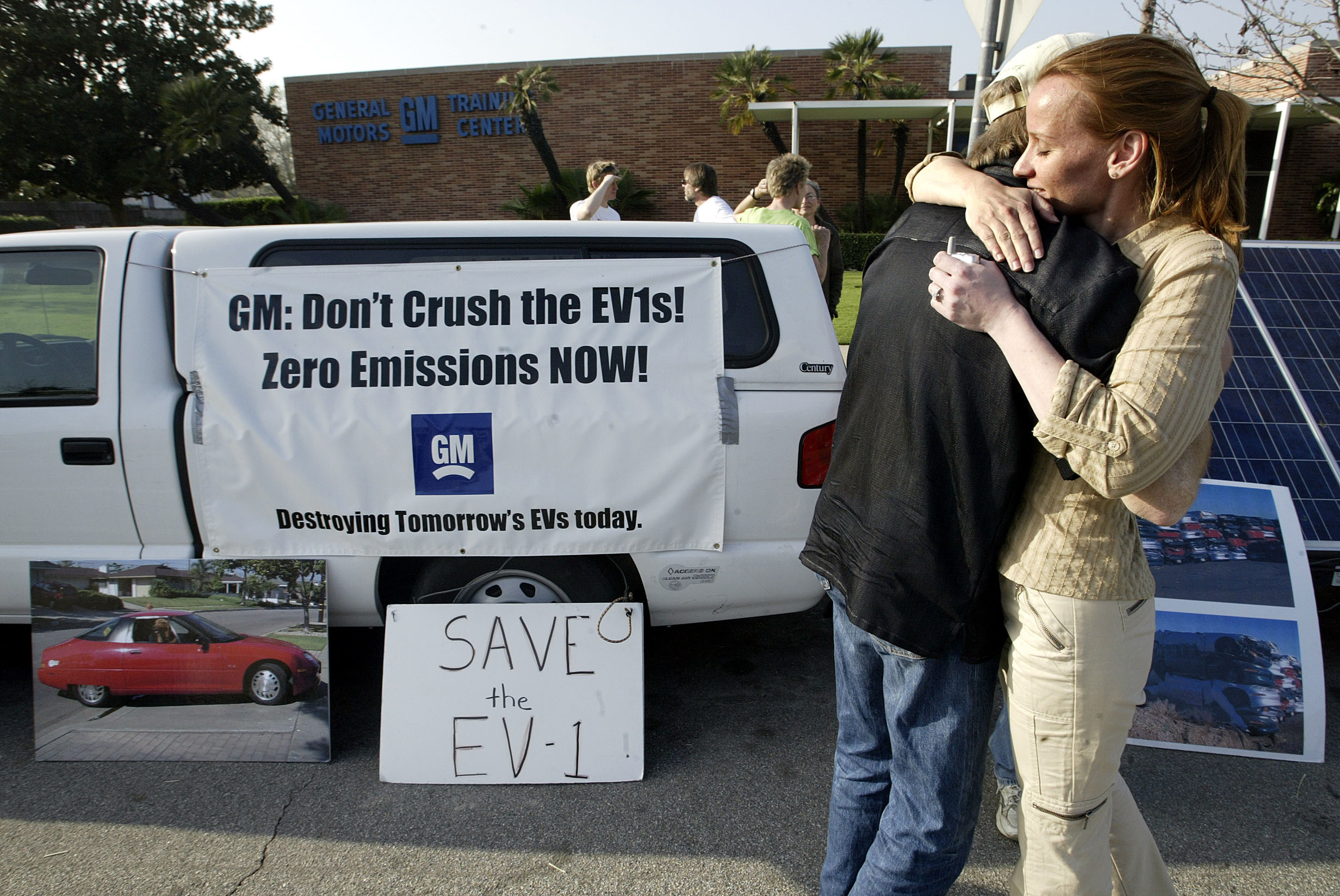 Chelsea Sexton, 29, hugs Paul Scott, 52, during a vigil held outside of the General Motors Training Center on Riverside Dr. in Burbank, protesting General Motors plans to crush around 70 EV1 electric vehicles that are currently located in parking lot at the Training Center. Sexton and Scott are 2 of the organizers for the vigil that started back on February 16 and has been held every day since, 24 hours a day. Photograph at far left is of a GM EV1 electric vehicle. (Photo by Mel Melcon/Los Angeles Times via Getty Images)
