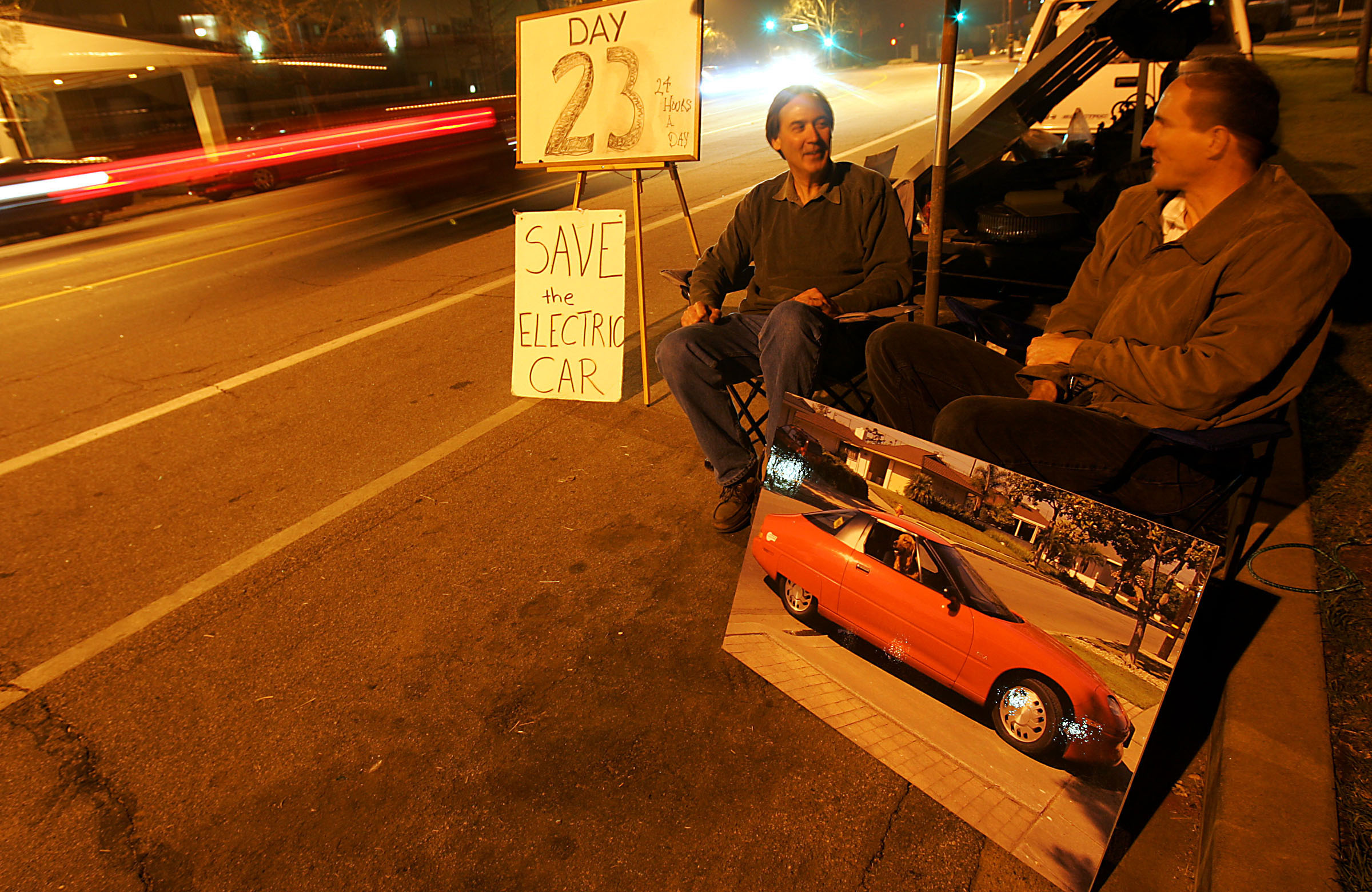 Mike Kane, left, and Earl Cox keep vigil in front of a General Motors facility in Burbank where the last few remaining EV1s are awaiting the scrap heap. Built and marketed in the 1990s, the EV1 is a rechargeable electrical coupe that can go from zero to 60 in eight seconds. (Photo by Luis Sinco/Los Angeles Times via Getty Images)